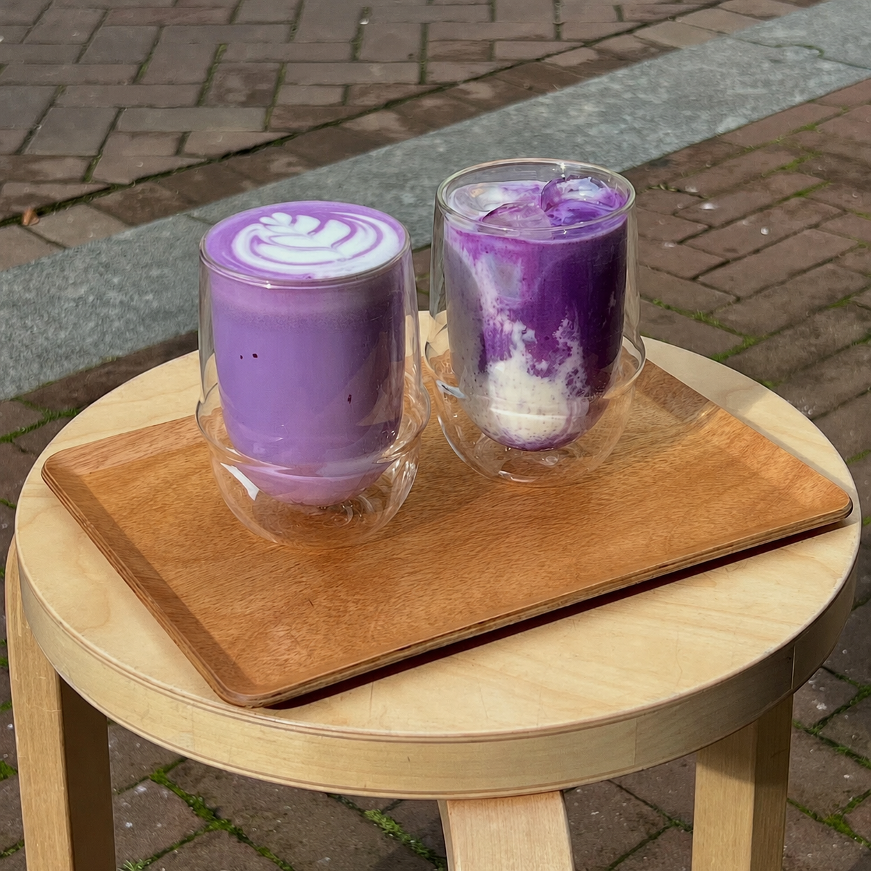 Two UBEST ube lattes on a wooden tray in warm daylight.