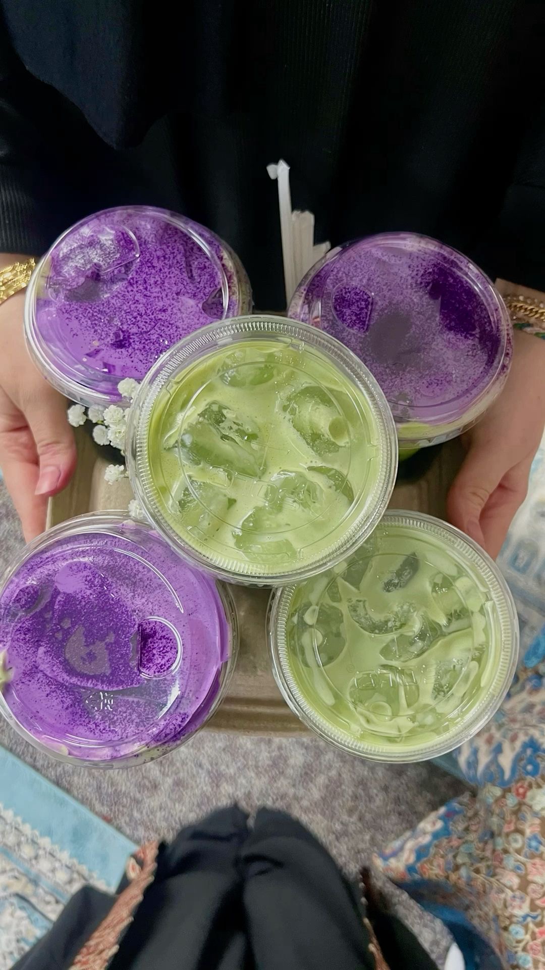 Overhead view of five iced ube and matcha lattes held between two hands.