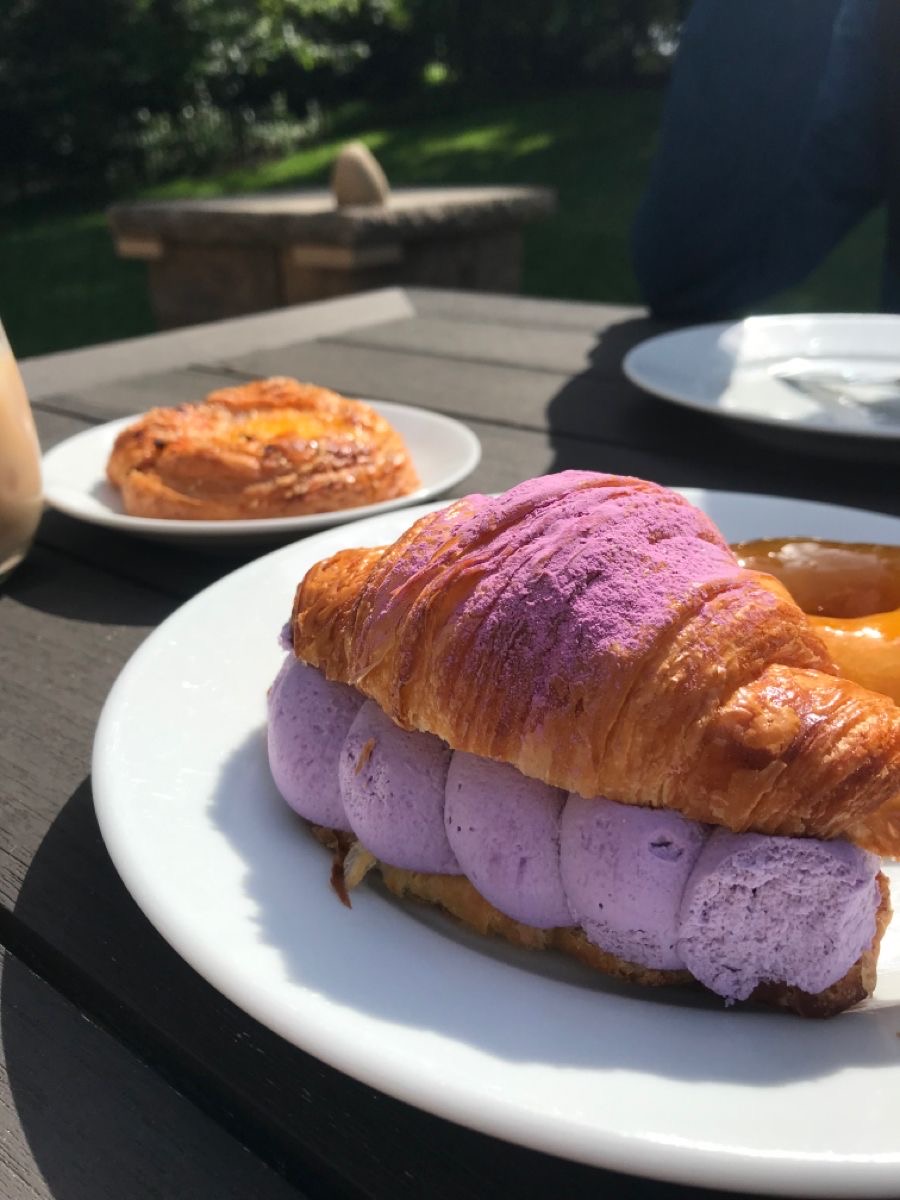 A flaky croissant filled with airy ube cream and dusted with purple ube powder, in warm sunlight.
